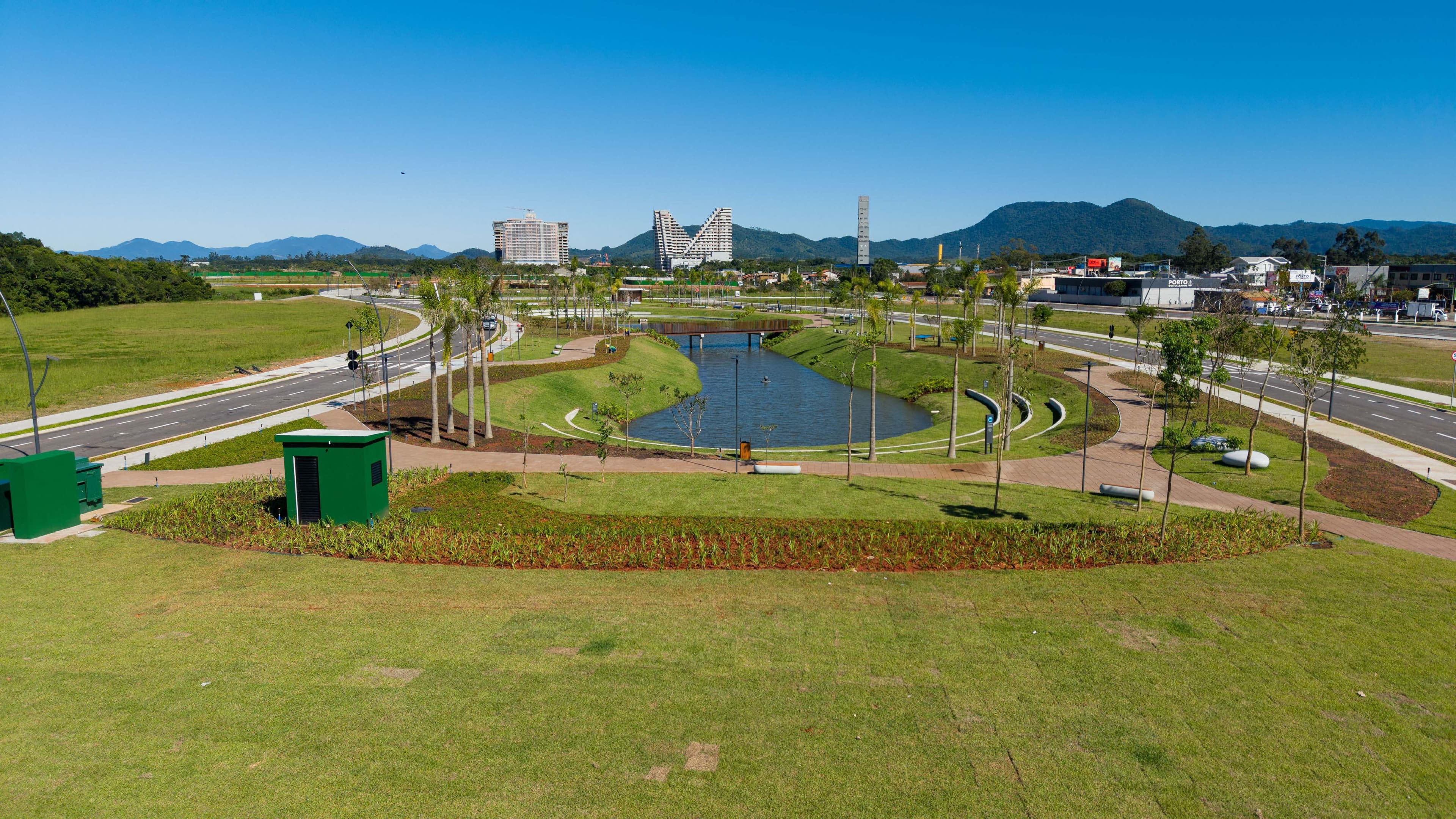 Vista aérea de parque urbano com lago, alamedas arborizadas, jardins e vias de acesso, com edifícios e montanhas ao fundo